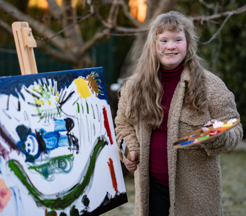 A teenage girl with Down Syndrome smiling and painting a mural.