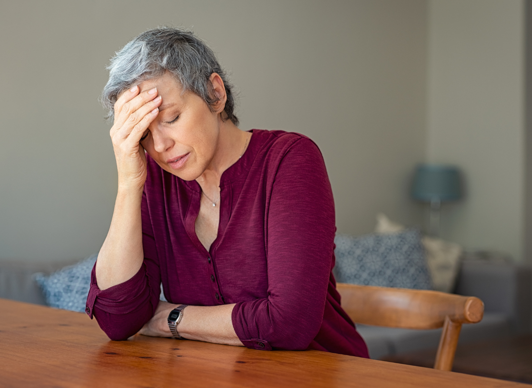 Lady with grey hair, stressed with her hand on her forehead.