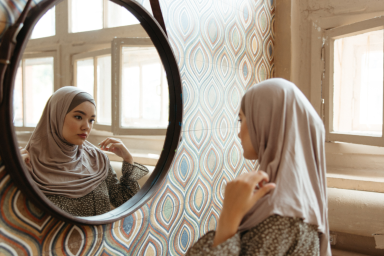 Woman wearing headscarf looks at her reflection in the mirror.