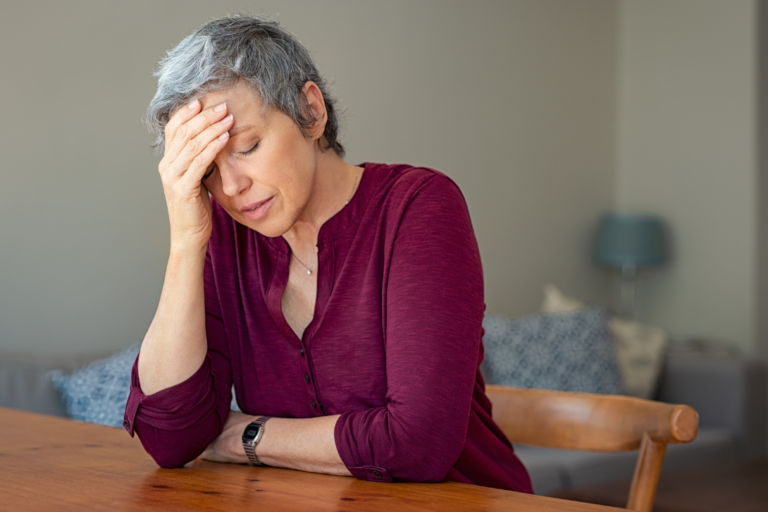 Lady with grey hair, stressed with her hand on her forehead.